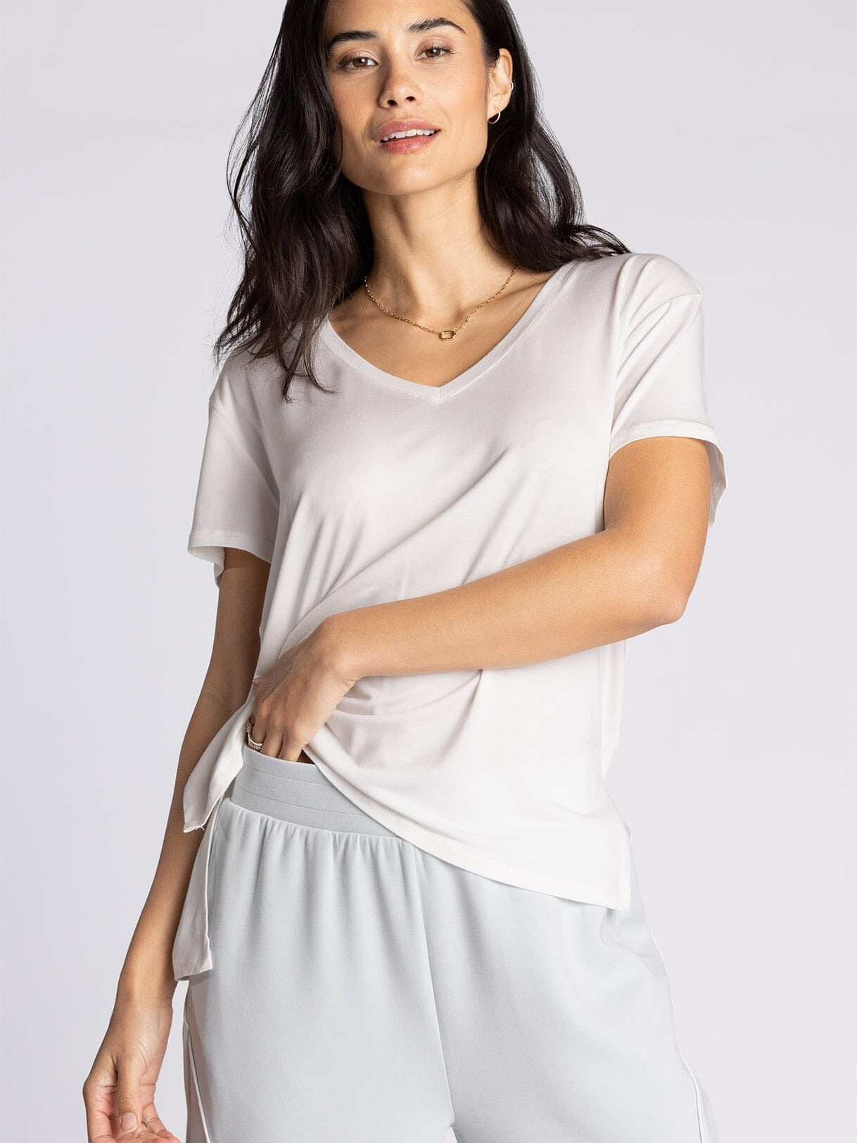 Woman wearing a white top and light gray pants on a plain background