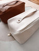 White clutch bag with gold zipper and hardware on a light surface.