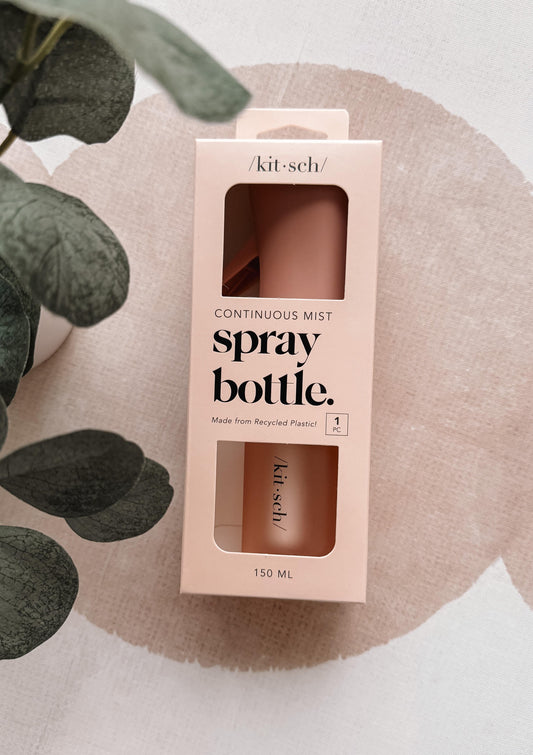 Kitsch spray bottle packaging on a textured surface with green leaves.