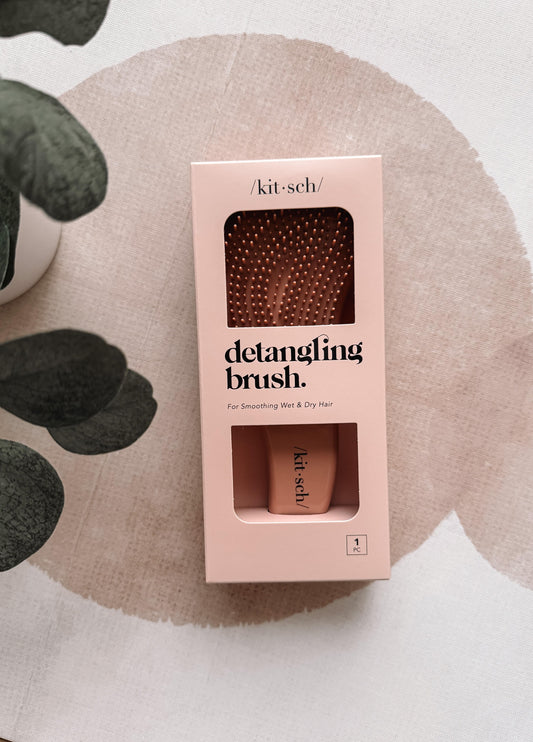 Kit & Sech detangling brush packaging on a textured surface with leaves.
