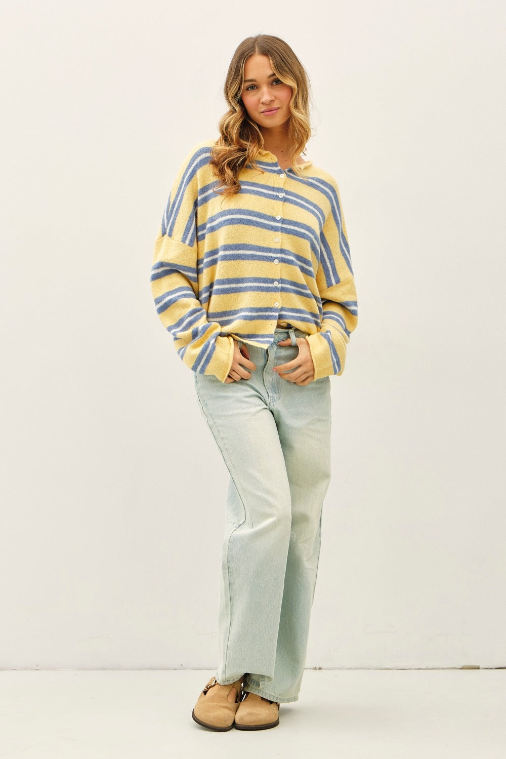Woman wearing a yellow and blue striped sweater with light blue jeans on a white background