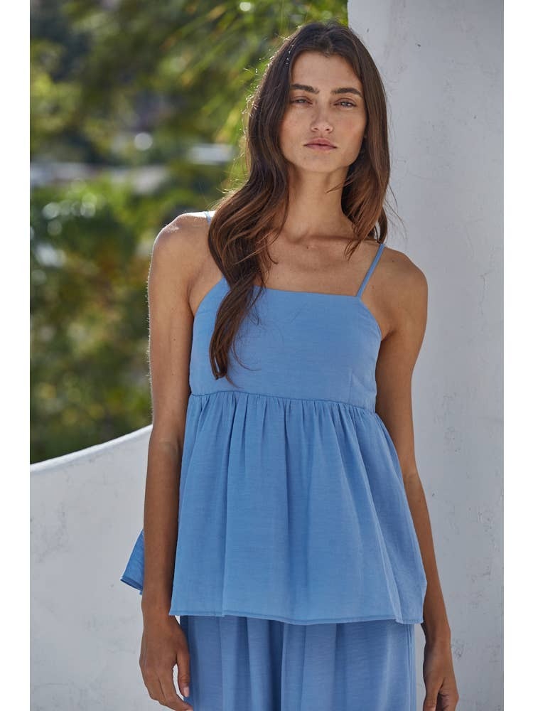 Woman wearing a blue dress standing against a white wall with greenery in the background
