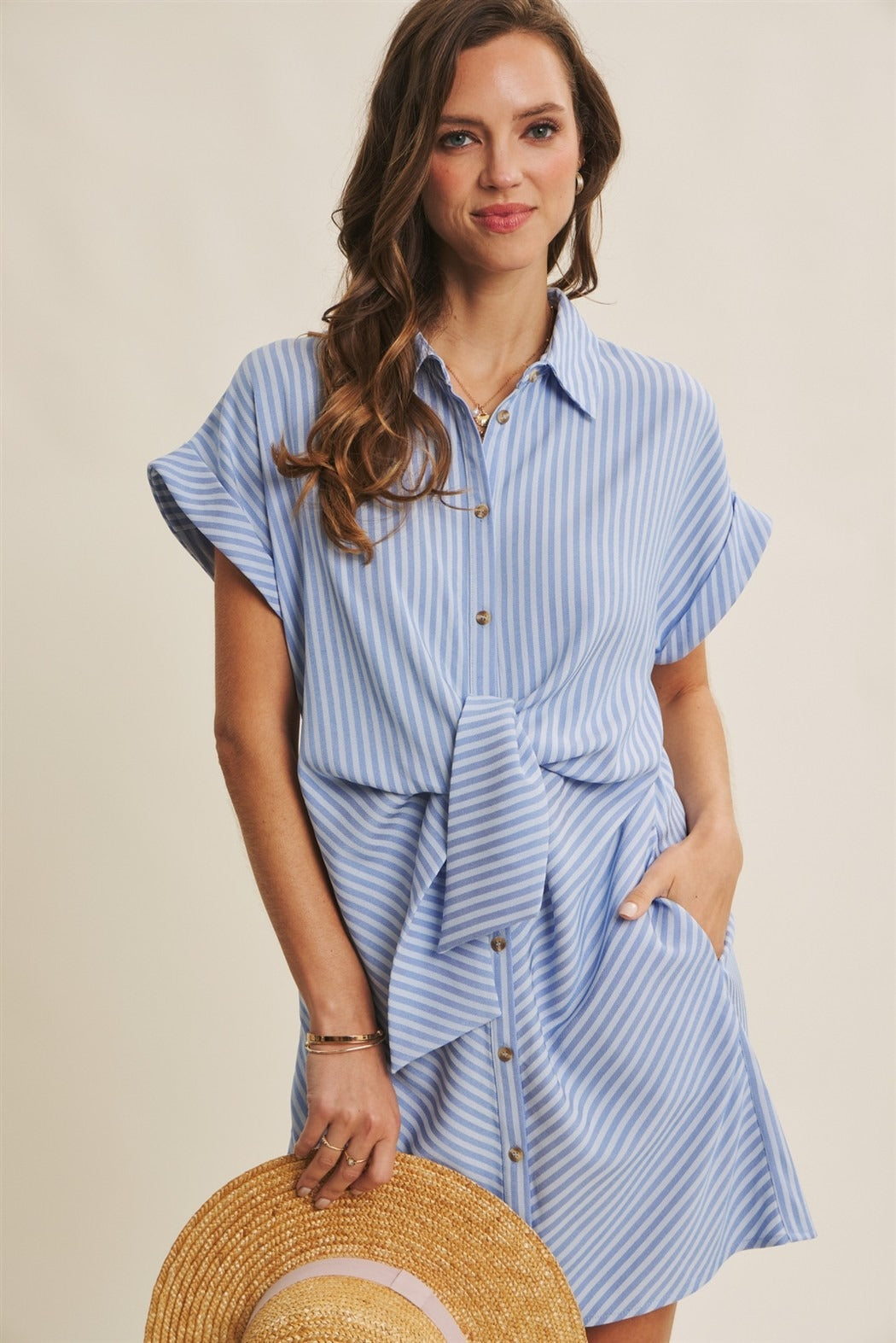 Woman wearing a blue striped dress holding a straw hat against a beige background