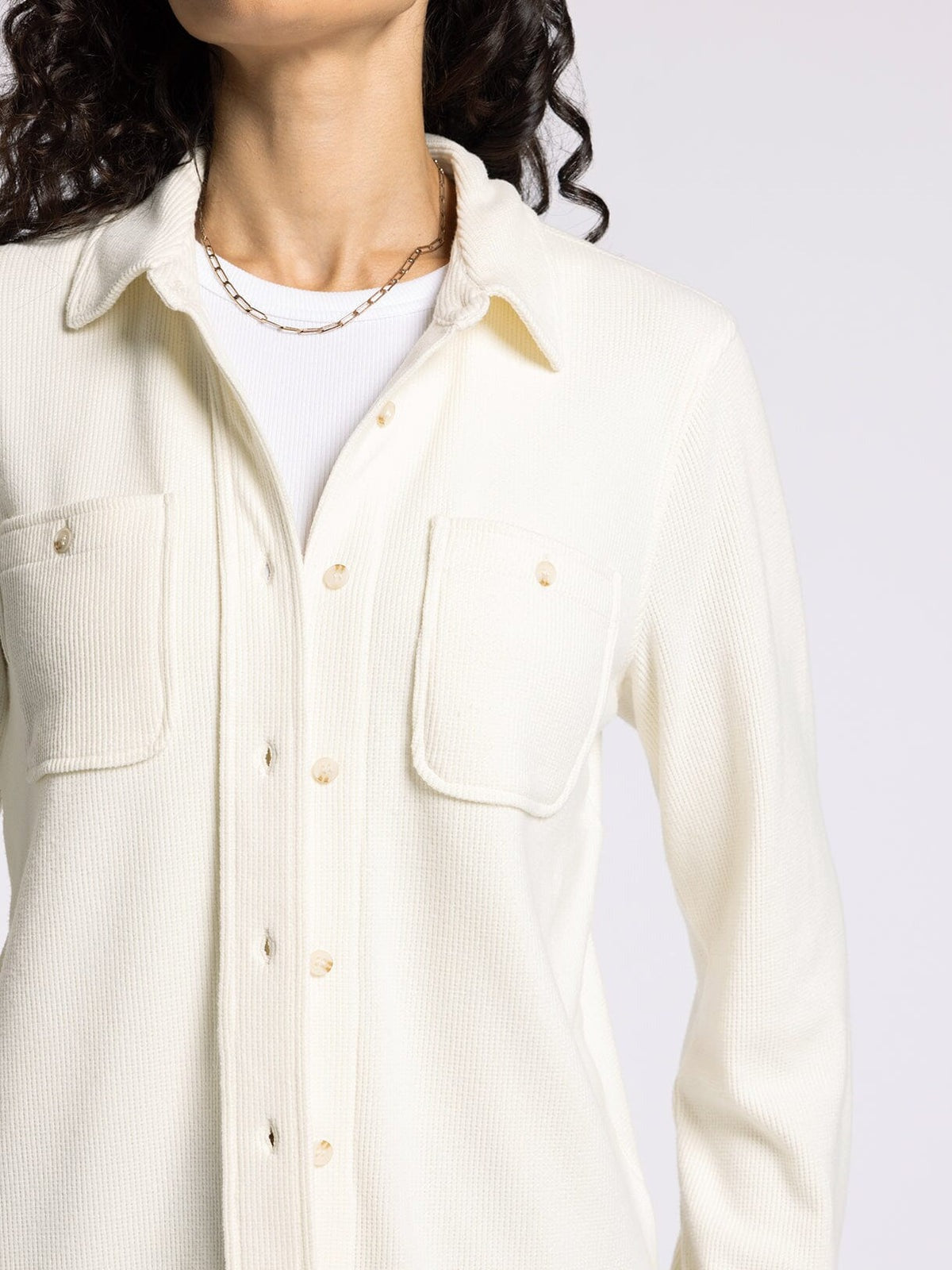 Close-up of a person wearing a cream-colored button-up shirt with a white background