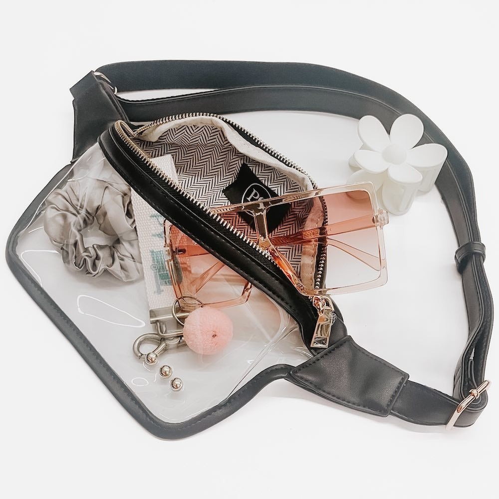 Black waist bag with clear compartment containing makeup items on a white background