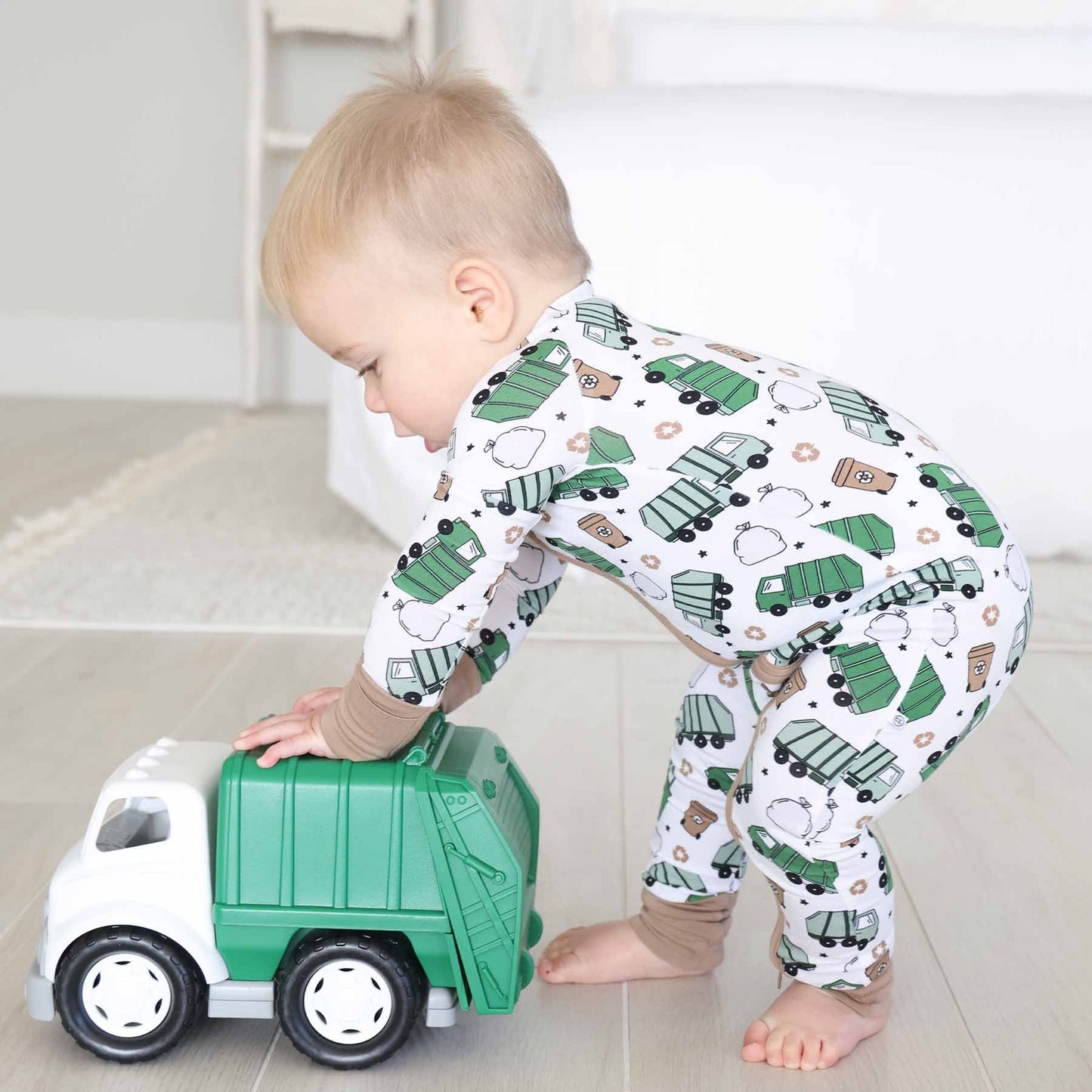 Child playing with a toy garbage truck wearing pajamas with vehicle patterns.