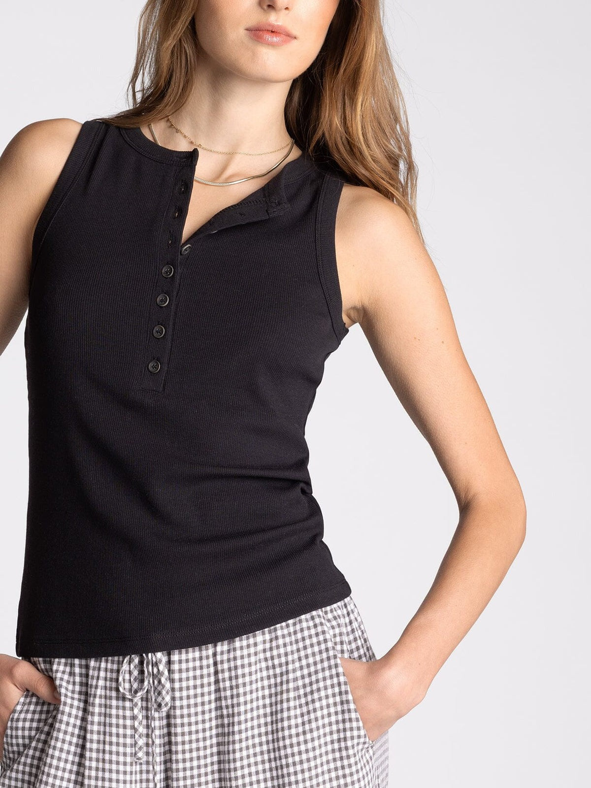 Woman wearing a black sleeveless shirt with buttons and a checkered skirt on a light gray background