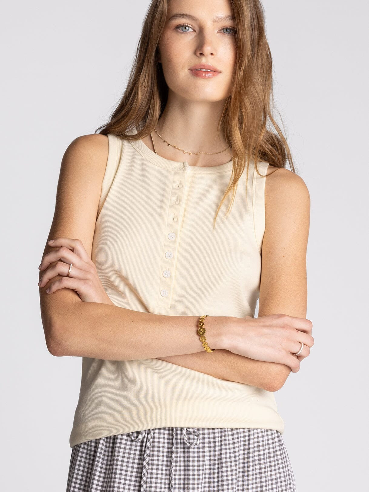 Woman wearing a beige sleeveless top with a plain background