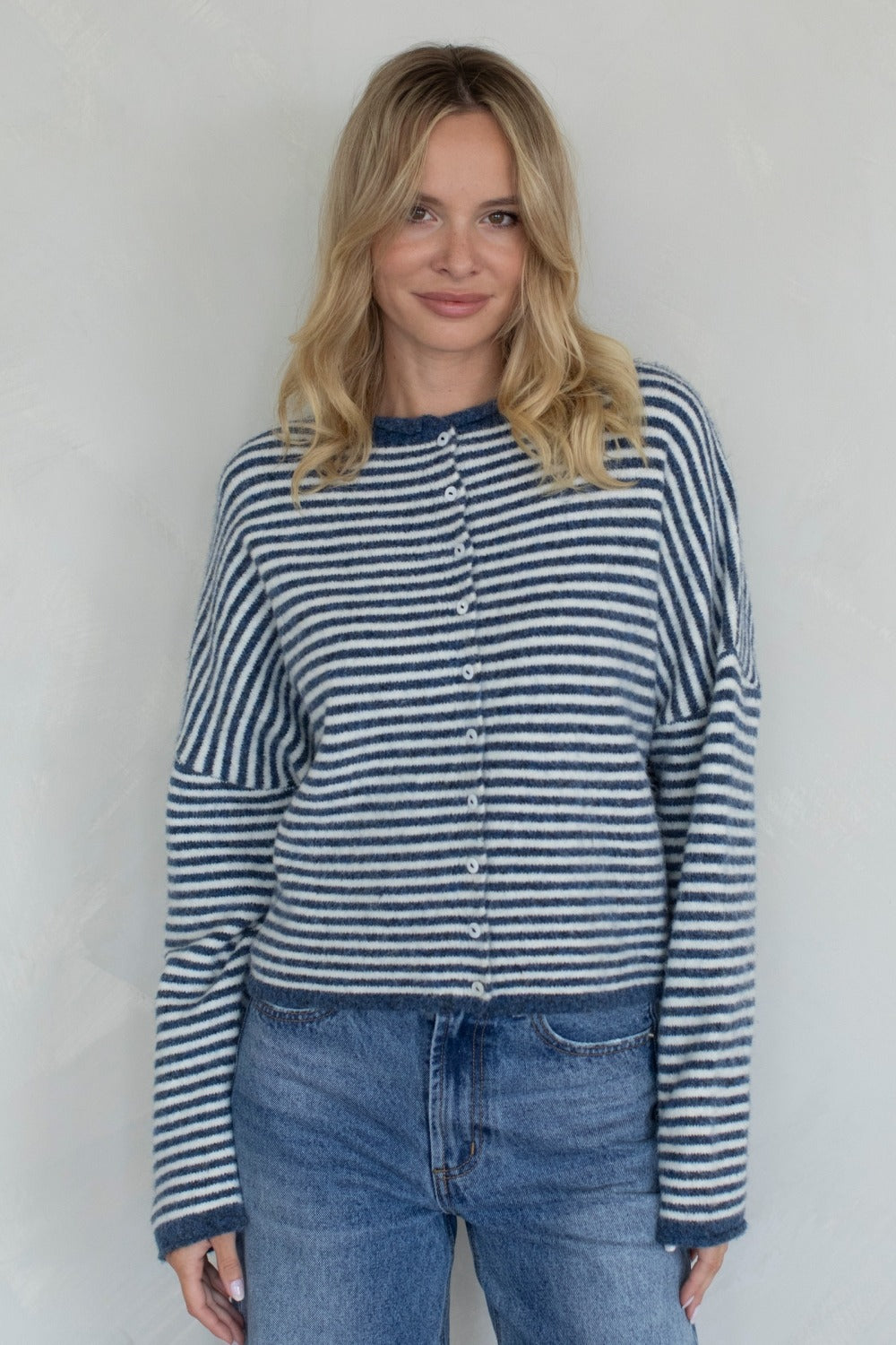 Woman wearing a blue and white striped shirt and jeans against a plain background