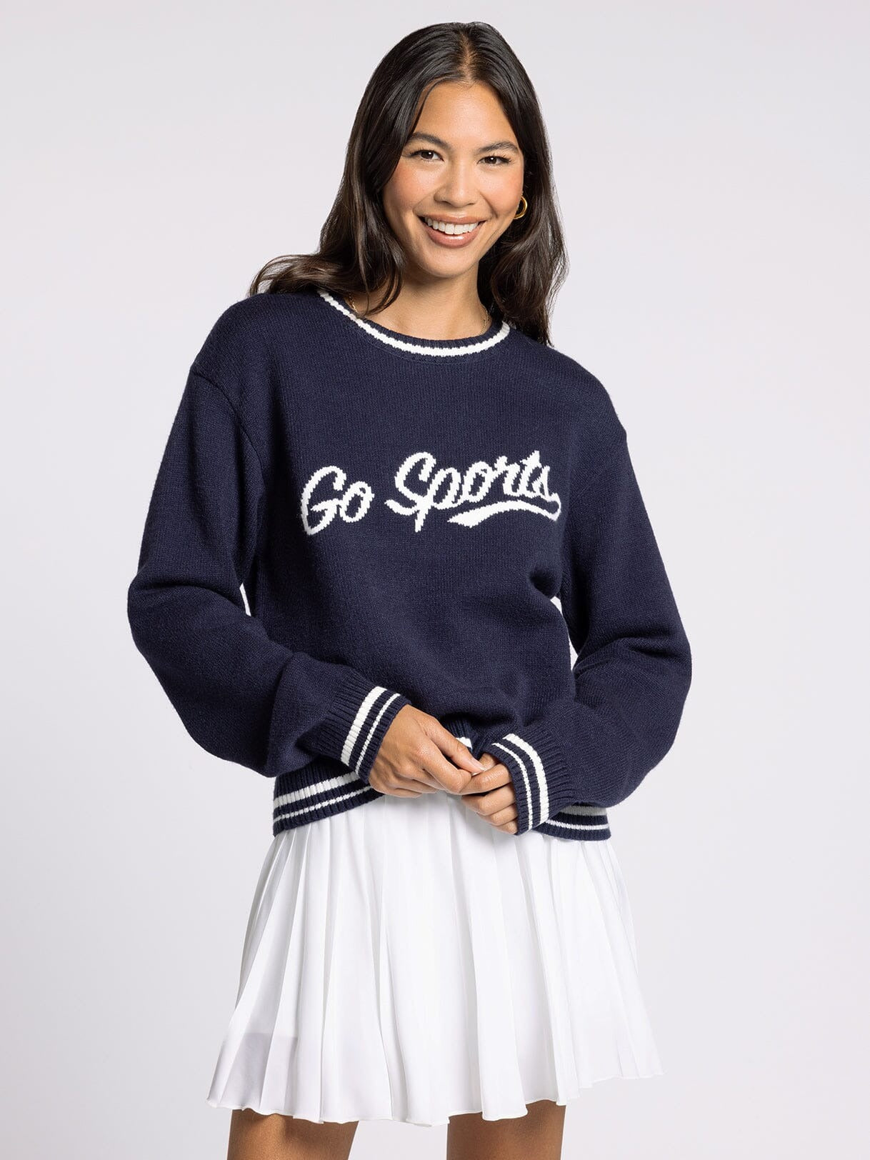 Woman wearing a navy sweater with 'Go Sports' text and a white skirt on a light gray background