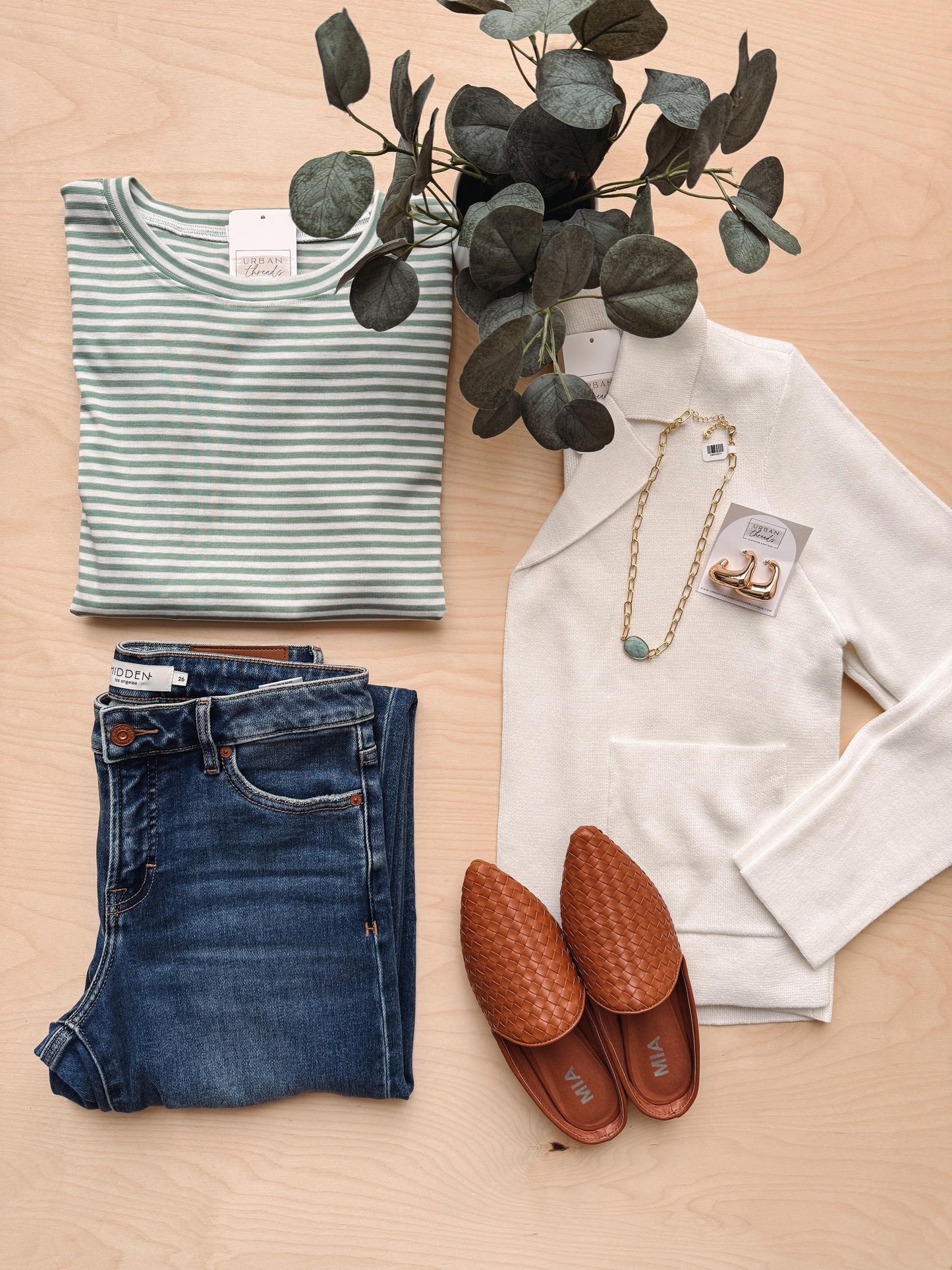 Striped shirt, jeans, white jacket, brown shoes, and a plant on a wooden surface