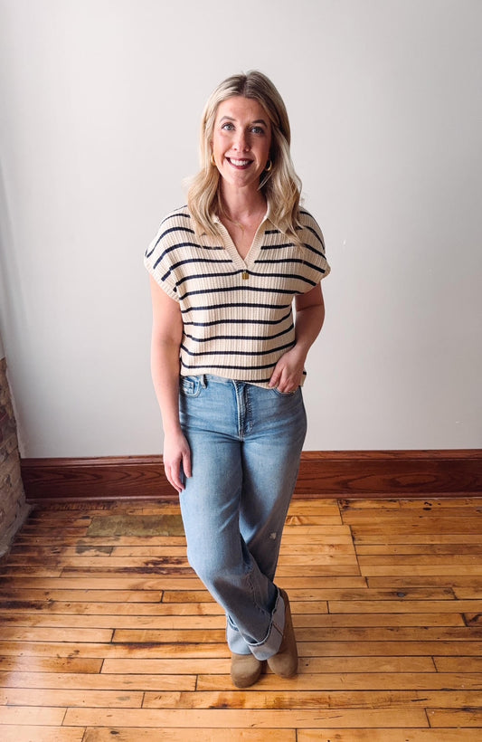 Woman wearing a striped shirt and jeans standing on a wooden floor.