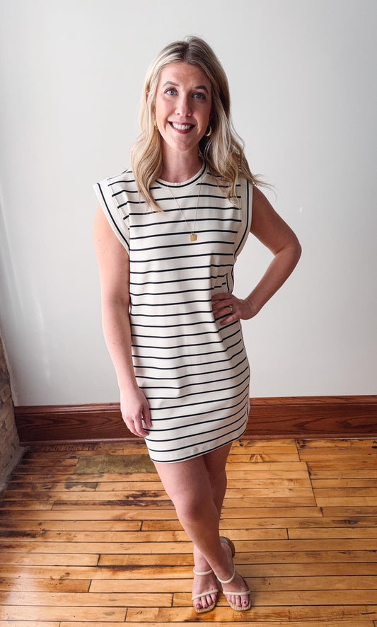 Woman wearing a striped dress standing on a wooden floor with a white wall background