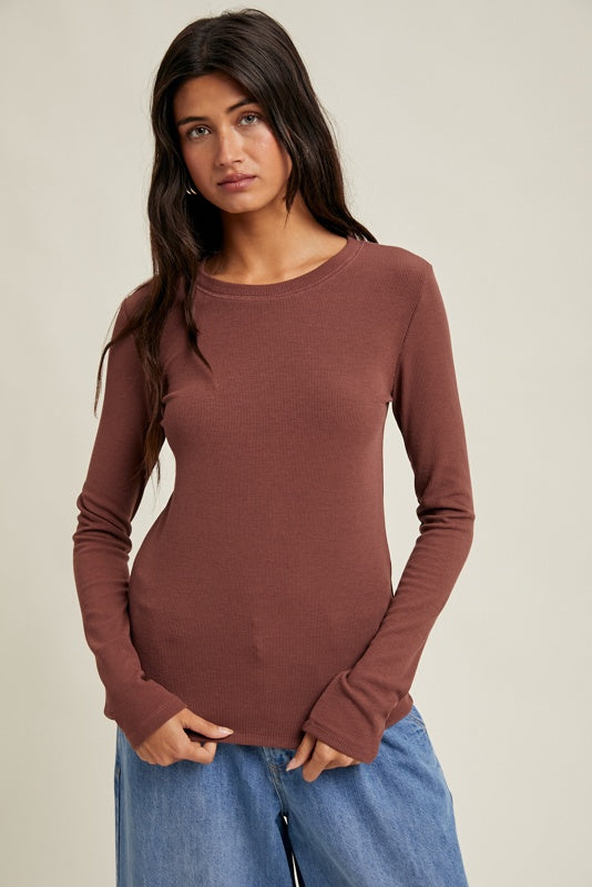 Woman wearing a brown long-sleeve top and blue jeans against a beige background