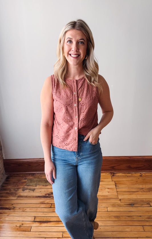 Woman wearing a pink sleeveless top and blue jeans standing on a wooden floor.