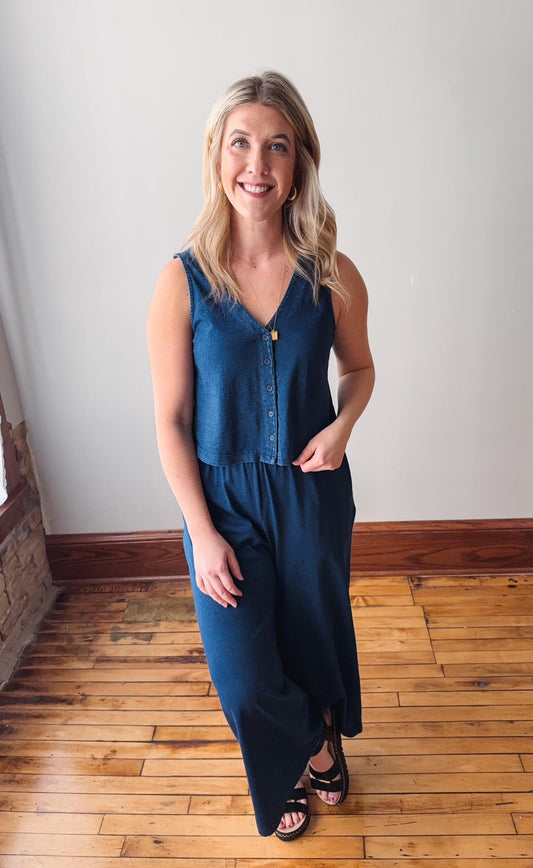 Woman wearing a blue jumpsuit standing on a wooden floor with a white wall background