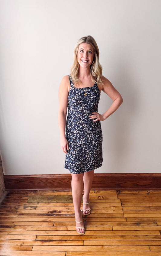 Woman wearing a floral dress standing on a wooden floor against a white wall