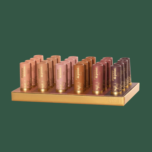 A display of Poppy & Pout lip tint tubes in various shades, arranged on a wooden stand against a green background.