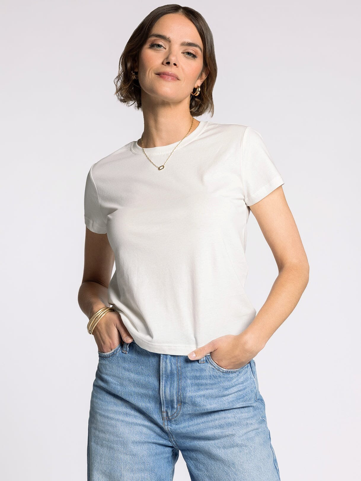 Woman wearing a white t-shirt and blue jeans against a plain background