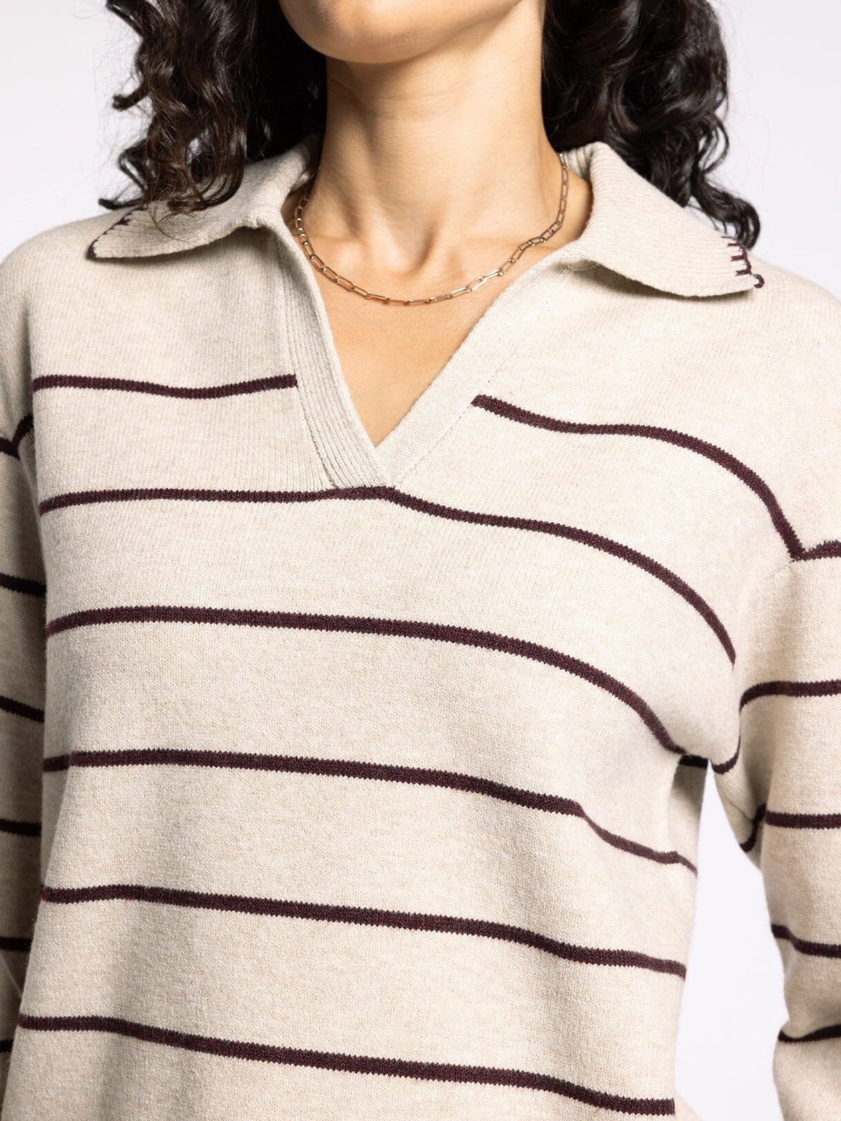 Close-up of a person wearing a cream sweater with burgundy stripes.
