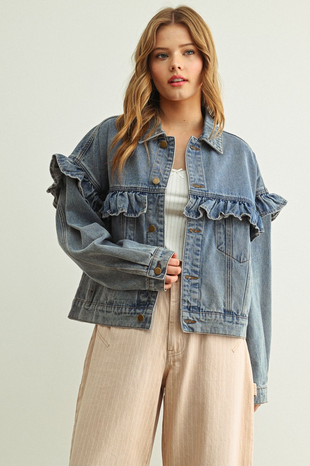 Woman wearing a denim jacket with ruffled details on a plain background