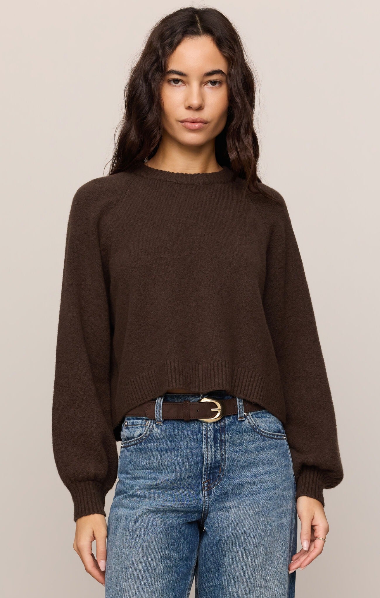 Woman wearing a brown sweater and blue jeans against a plain background
