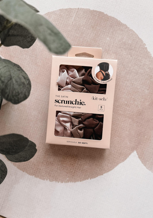 Package of satin scrunchies on a textured surface with green leaves.