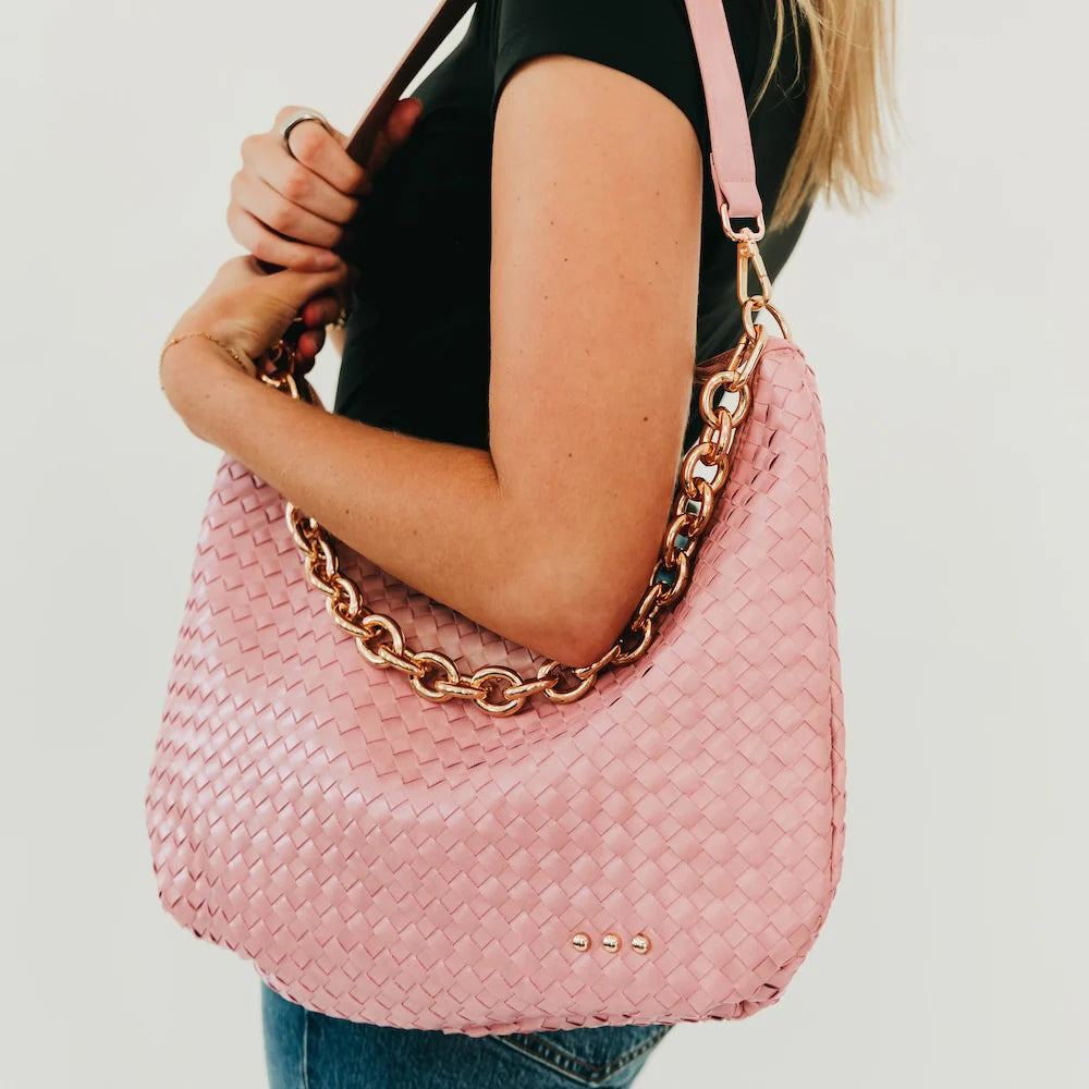 Pink handbag with chain detail held by a person on a plain background