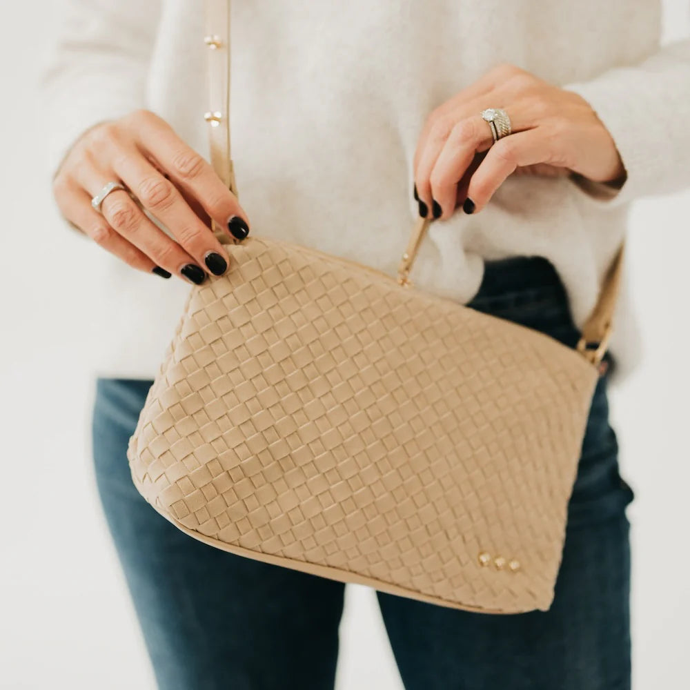 Beige woven handbag held by a person wearing a white sweater and dark pants.