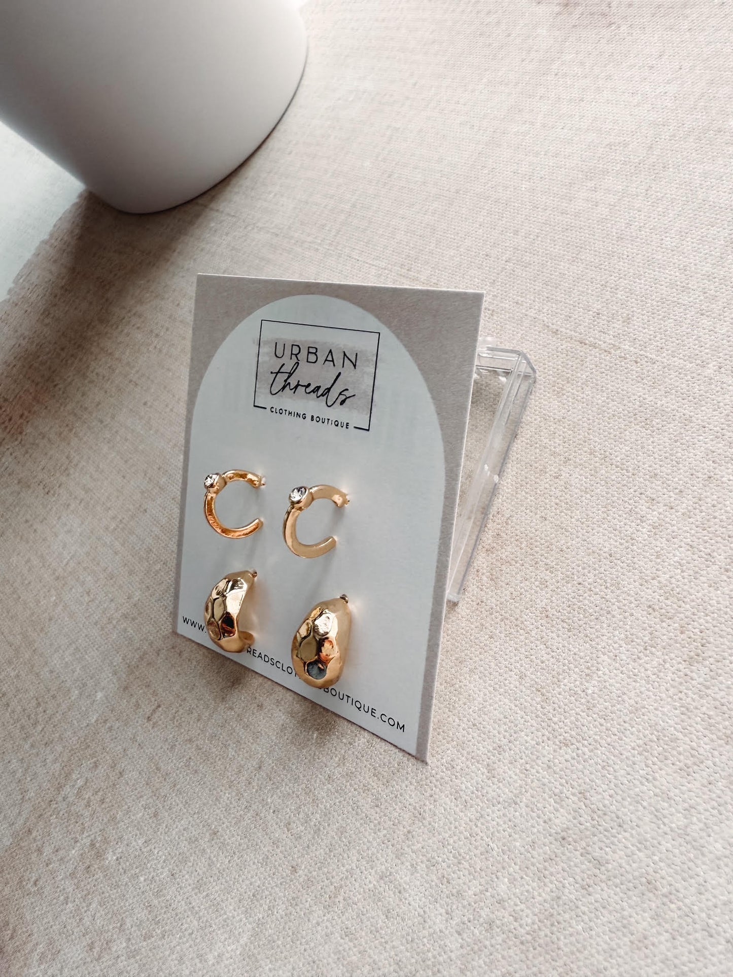 Gold earrings on a card with 'Urban Threads' branding on a light surface.