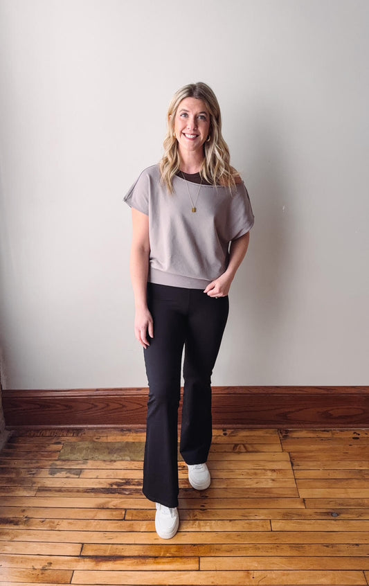 Woman wearing a gray t-shirt and black pants standing on a wooden floor with a white wall background