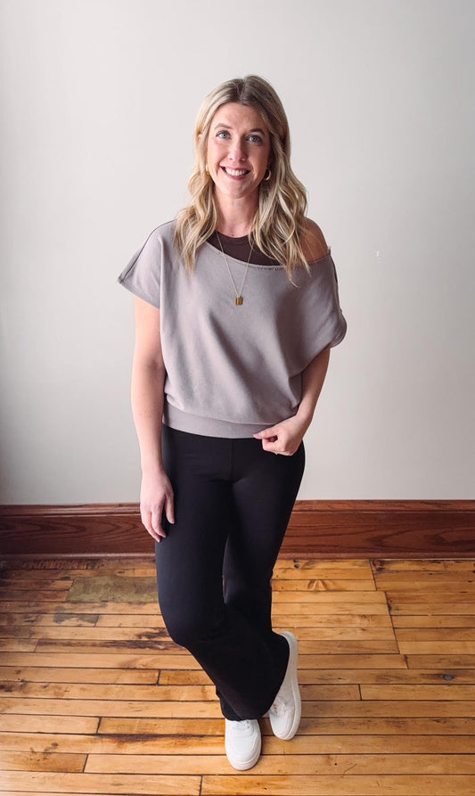 Woman wearing a gray off-shoulder top and black leggings on a wooden floor.