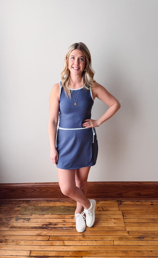 Woman wearing a blue dress standing on a wooden floor with a white wall background