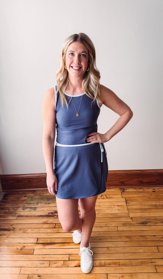 Woman wearing a blue dress standing on a wooden floor with a white wall background