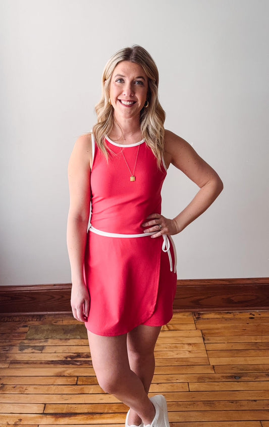 Woman wearing a red dress standing on a wooden floor with a white wall background