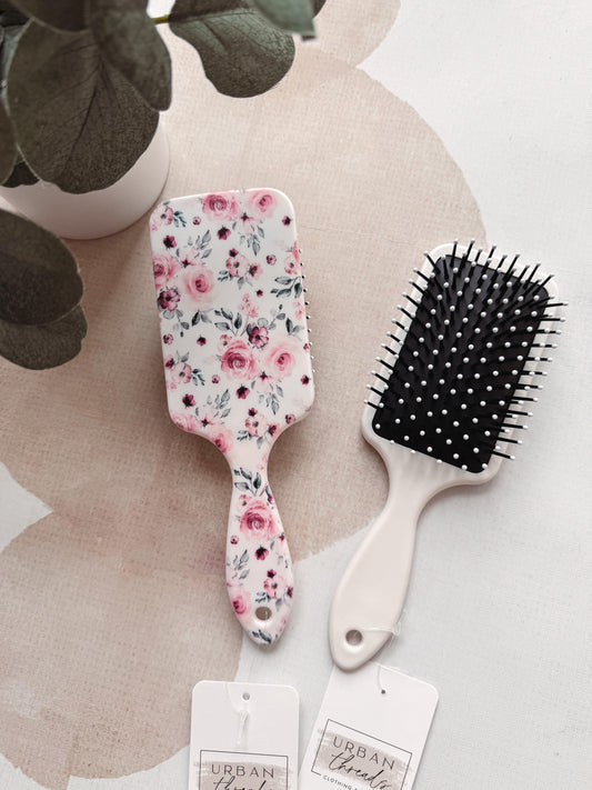 Two hairbrushes with floral design and black bristle brush on a neutral background