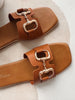 Pair of brown sandals with gold buckles on a light background