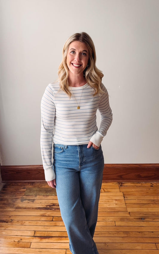 Woman wearing a striped sweater and jeans standing on a wooden floor.