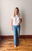 Woman wearing a white t-shirt and blue jeans standing against a plain wall.