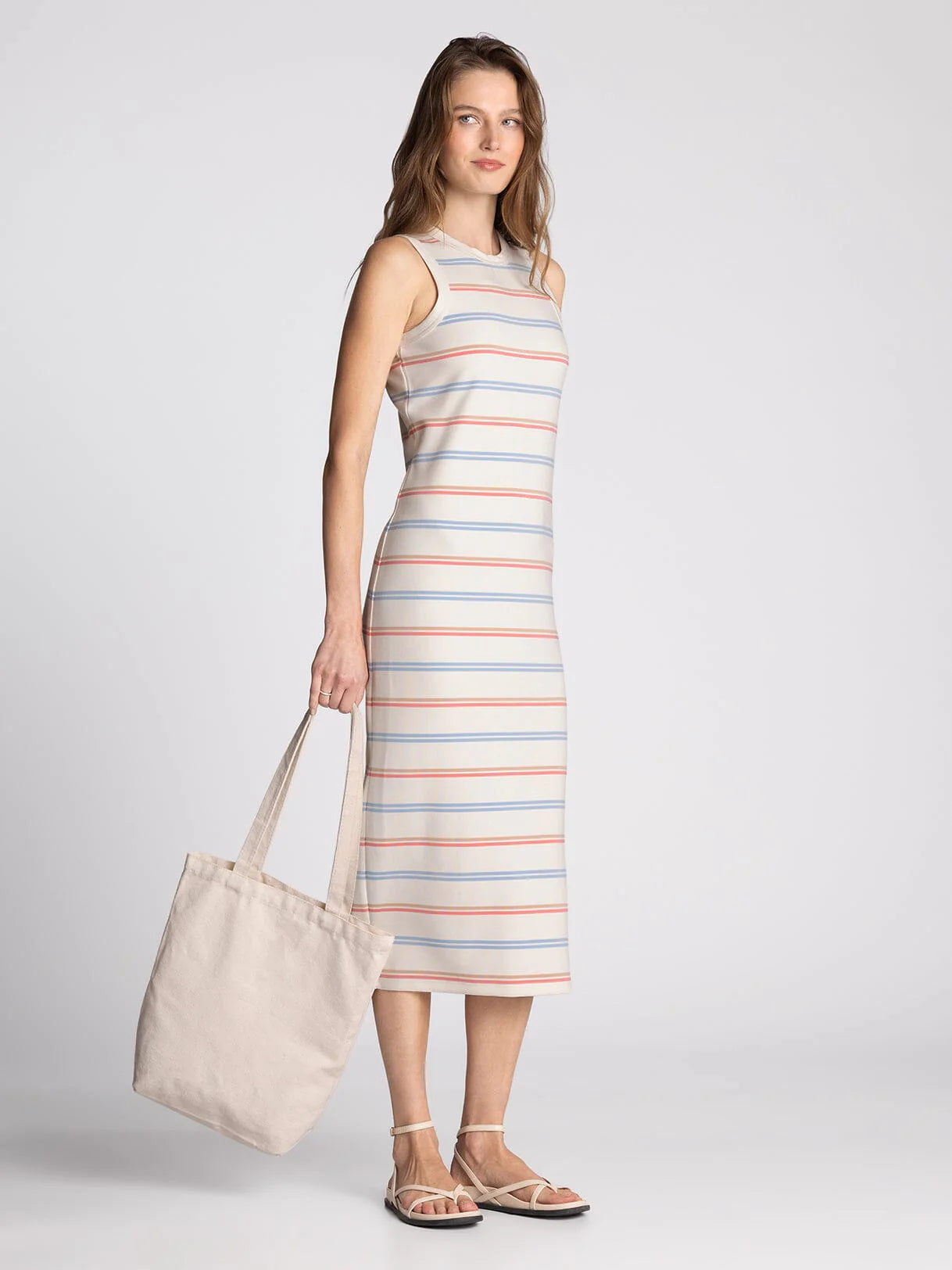 Woman wearing a striped dress holding a tote bag on a plain background
