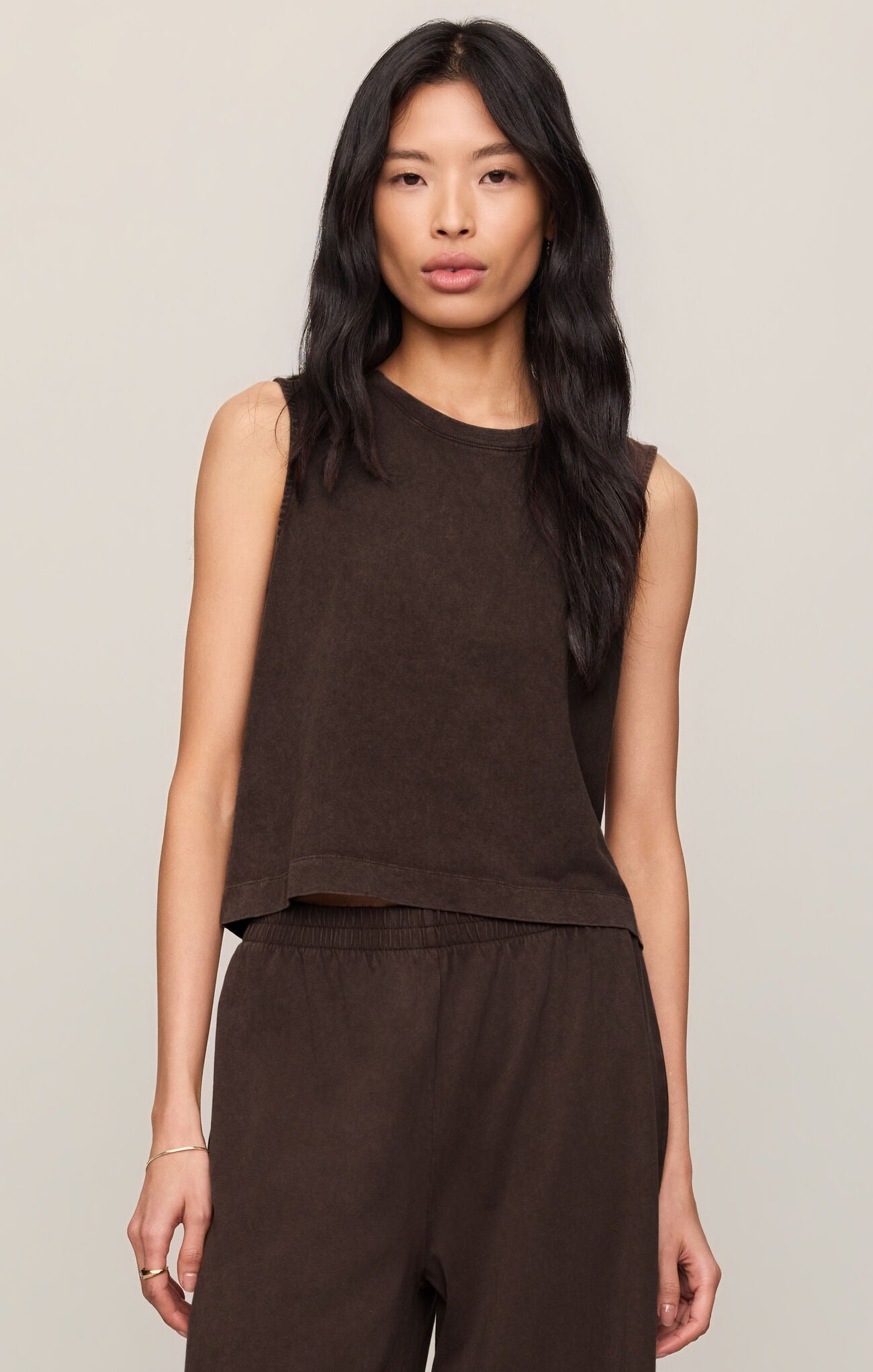 Woman wearing a brown sleeveless top and pants against a neutral background