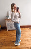 Woman taking a mirror selfie wearing a gray sweater and blue jeans in a room with wooden flooring and a decorative cabinet.