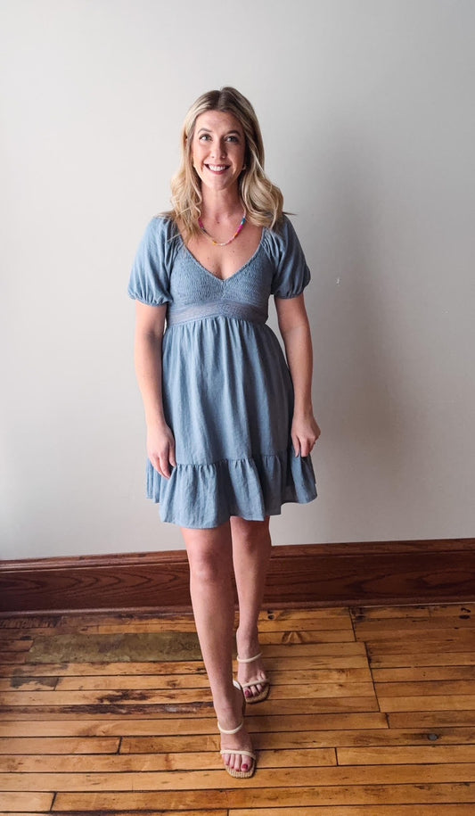 Woman wearing a blue dress standing on a wooden floor against a white wall
