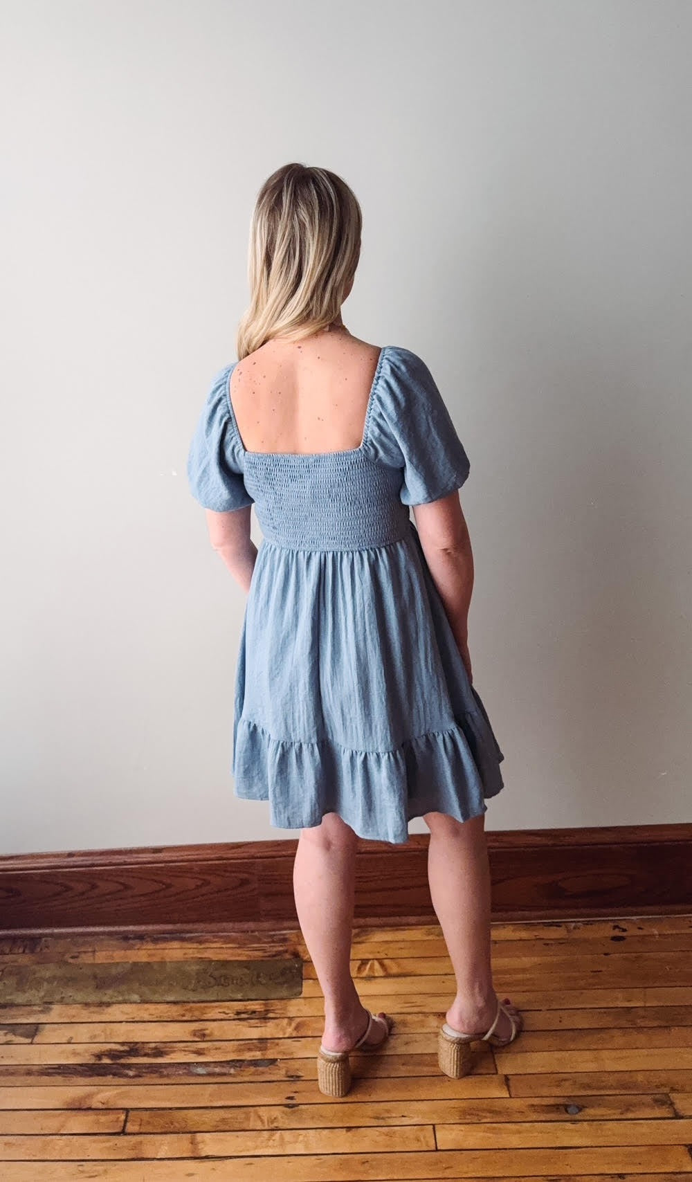 Woman wearing a blue dress standing on a wooden floor with a plain wall background