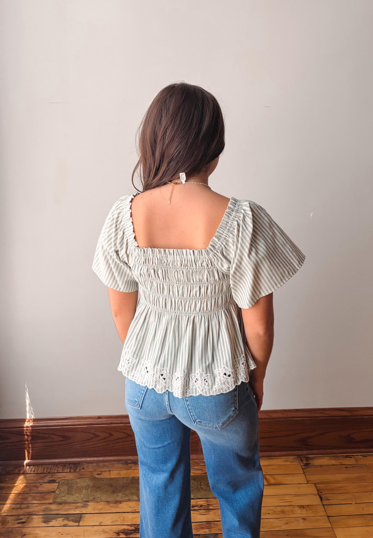 Person wearing a light-colored peplum top and blue jeans against a plain wall.