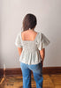 Person wearing a light-colored peplum top and blue jeans against a plain wall.