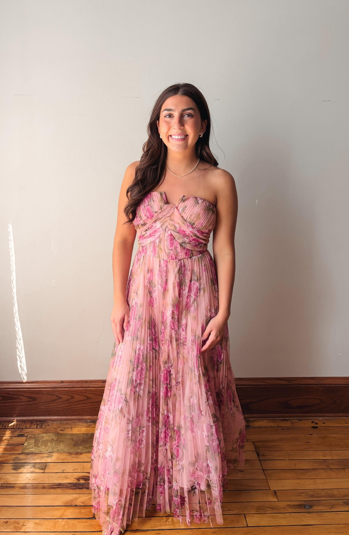 Woman wearing a pink floral dress standing against a plain wall.