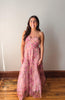Woman wearing a pink floral dress standing against a plain wall.