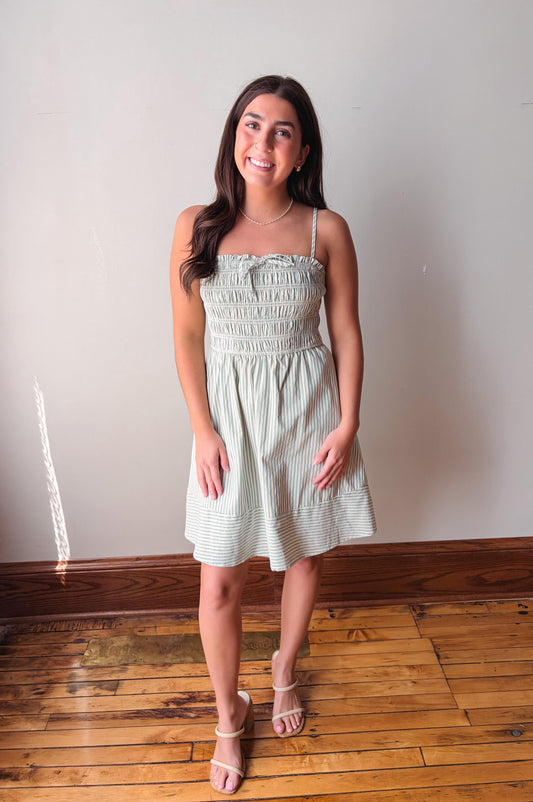 Woman wearing a light green dress standing on a wooden floor with a white wall background