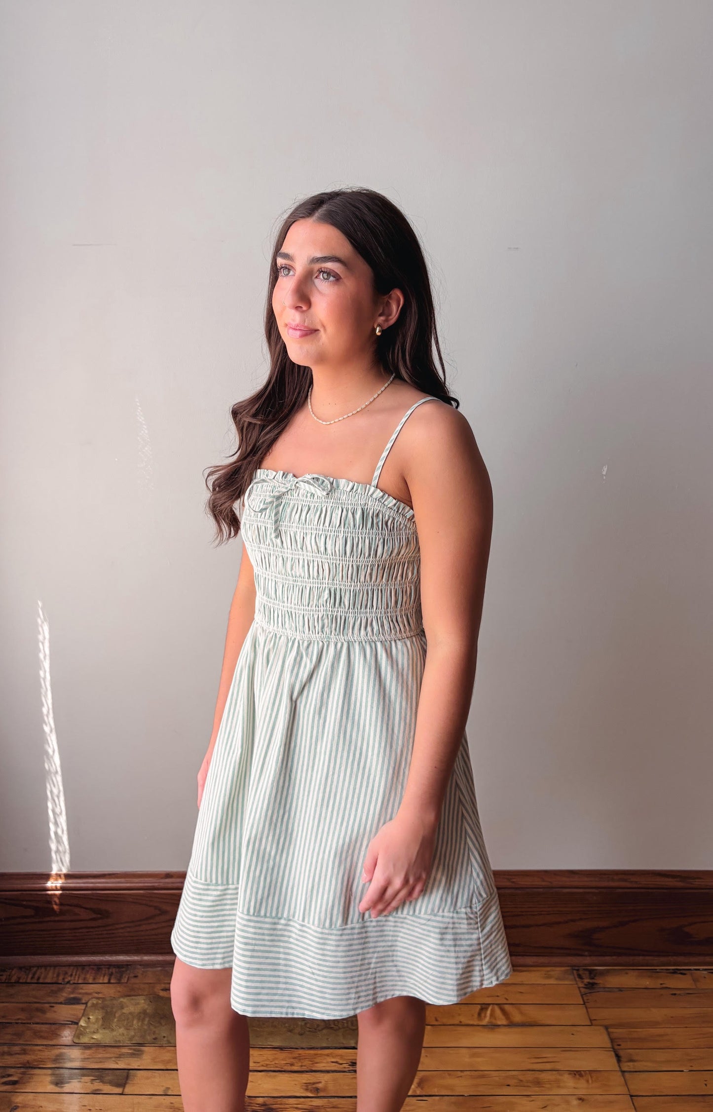 Woman wearing a light green dress standing against a plain wall.